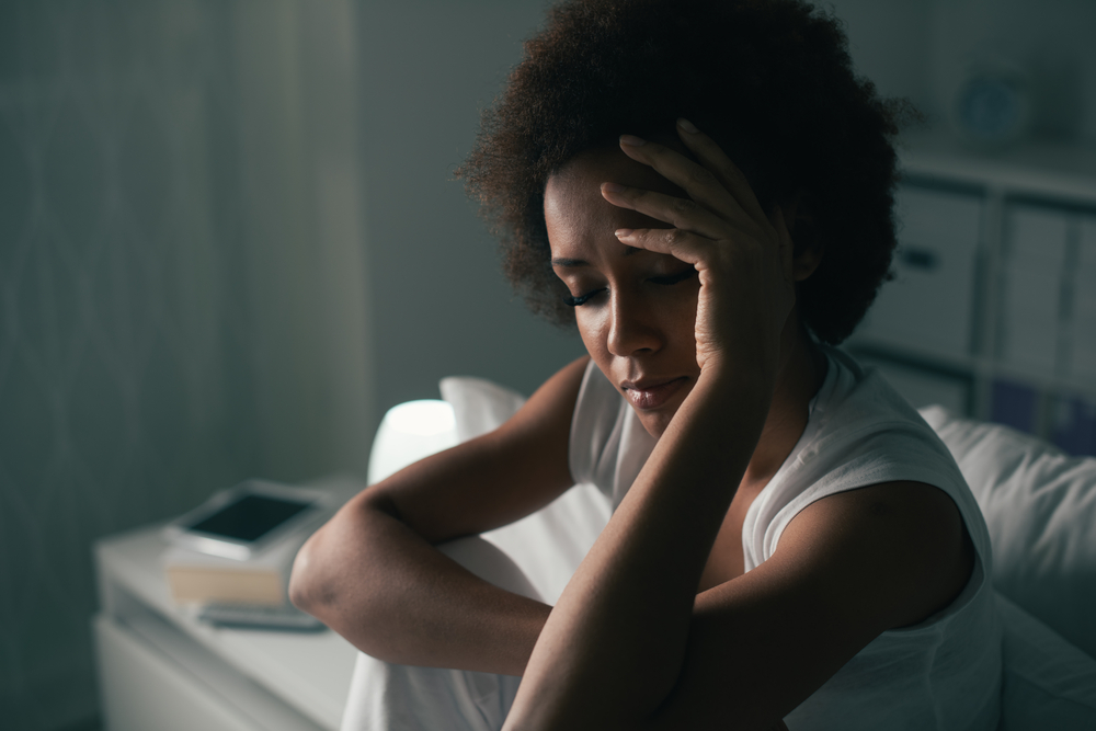 Sad depressed woman suffering from insomnia, she is sitting in bed and touching her forehead, sleep disorder and stress concept
