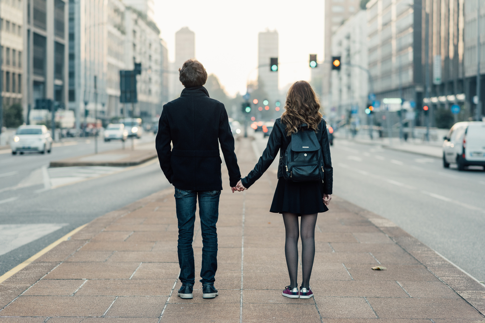 Back view of young beautiful couple in love hand in hand walking outdoor in the city, having fun - first date, romantic, love concept