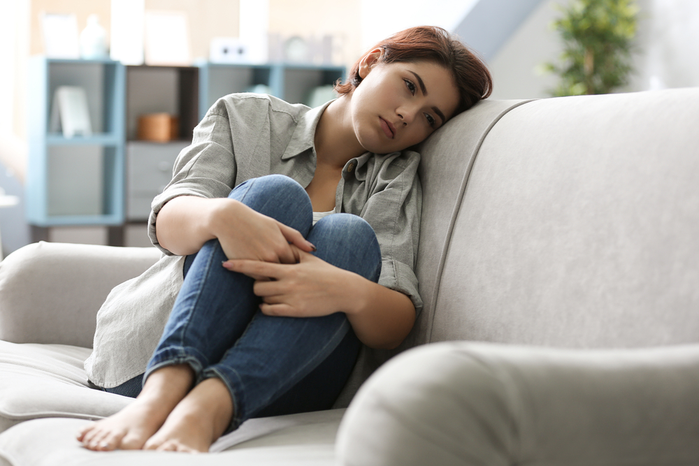 Depressed young woman sitting on sofa at home
