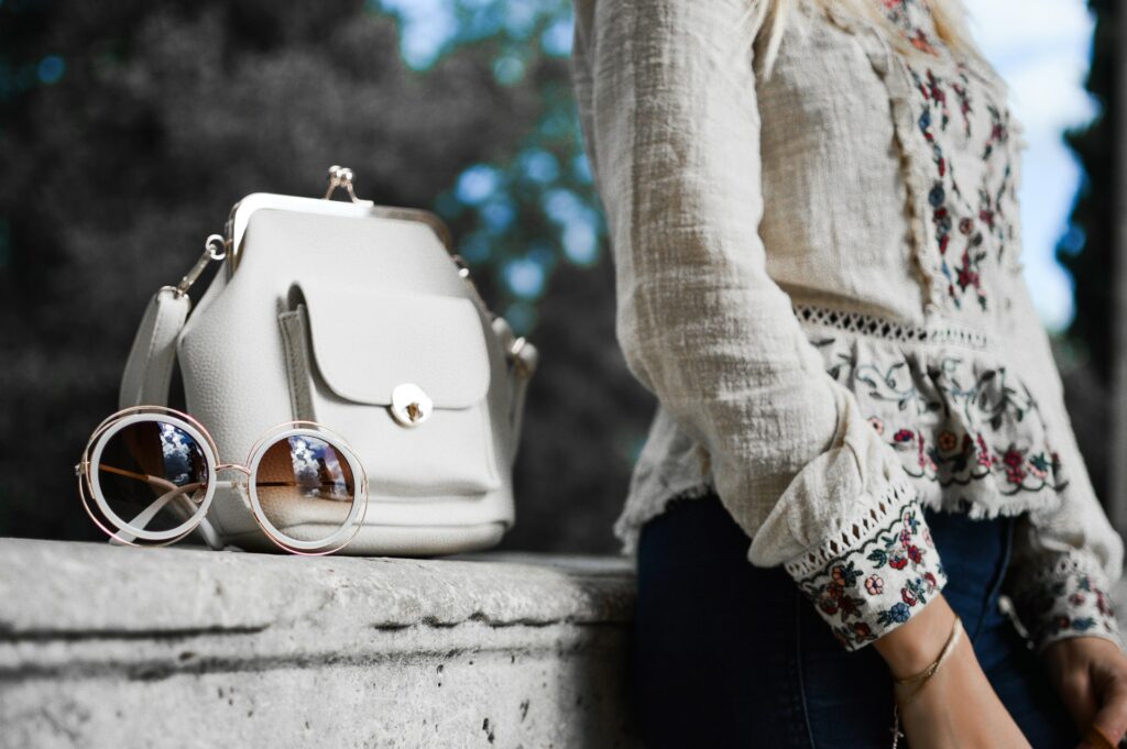woman wearing beige and red floral top leaning on gray concrete slab with white leather bag ontop
