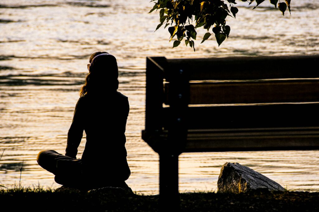 silhouette of person sitting on bench near body of water during daytime
