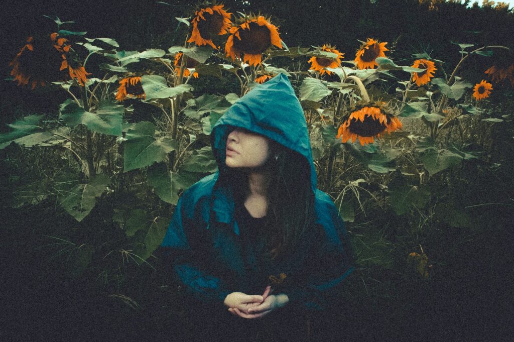a woman in a blue hoodie sitting in a field of sunflowers
