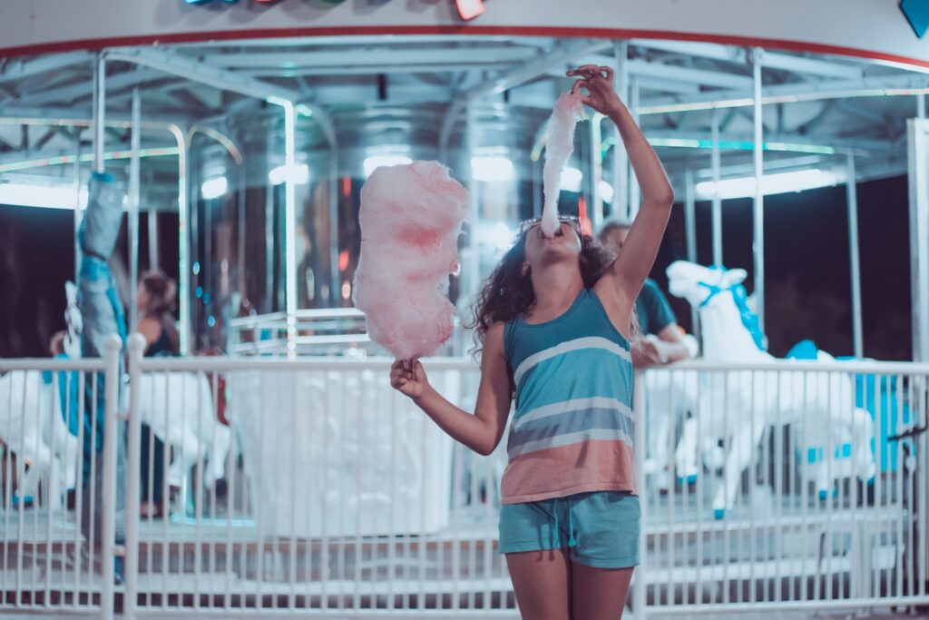 woman eating pink cotton candy beside carousel
