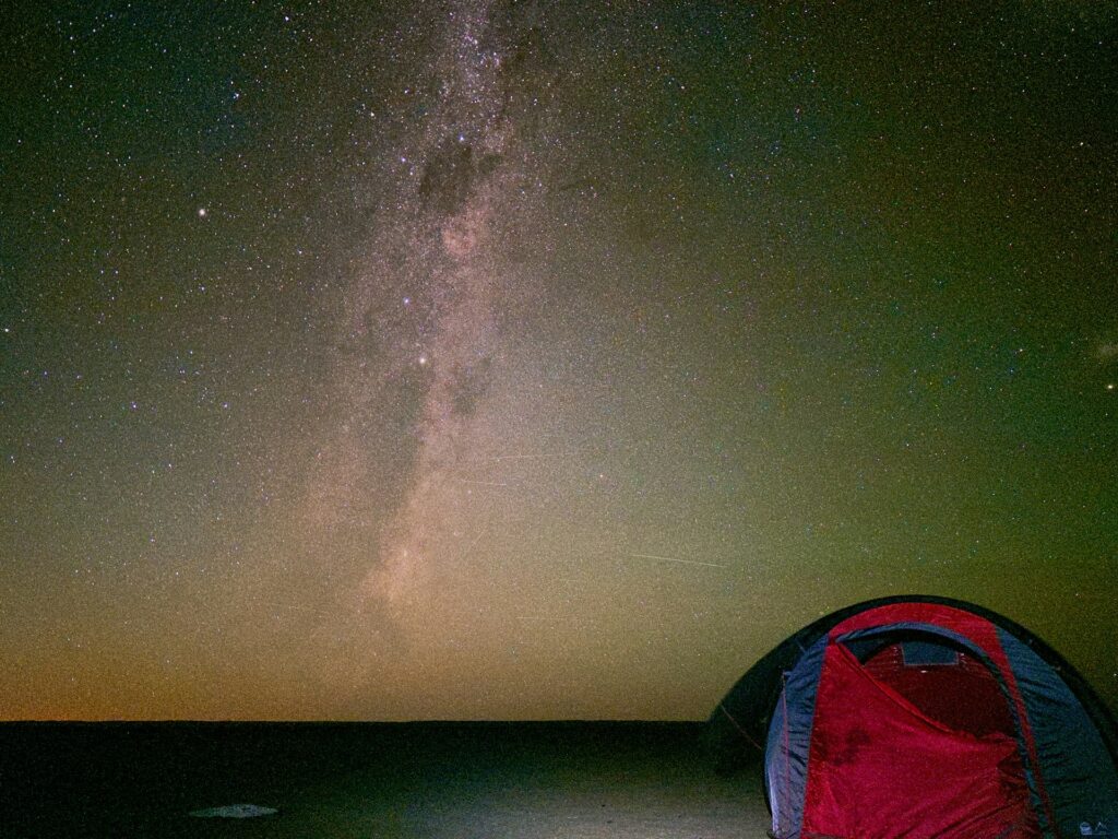 a tent pitched up on a beach under a night sky filled with stars