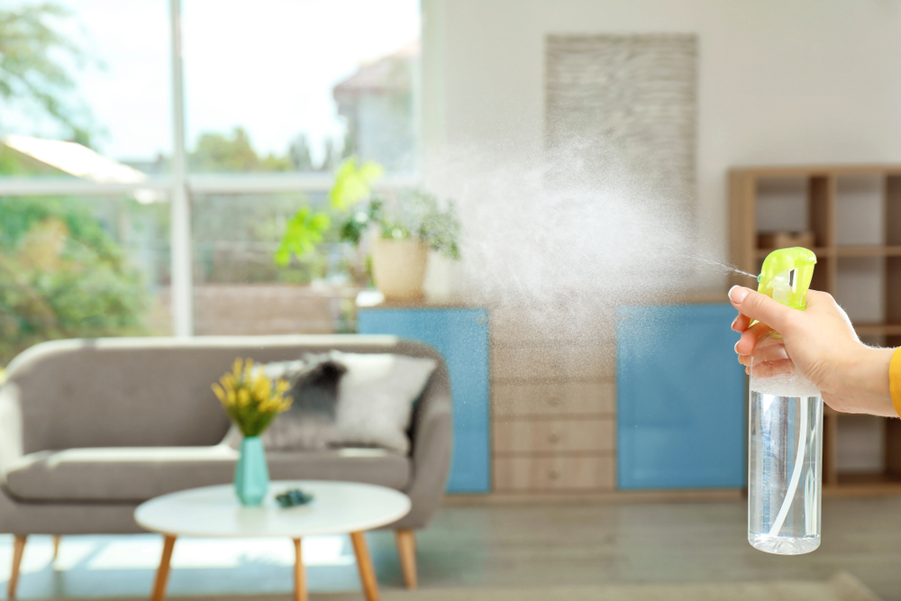 Woman spraying air freshener at home