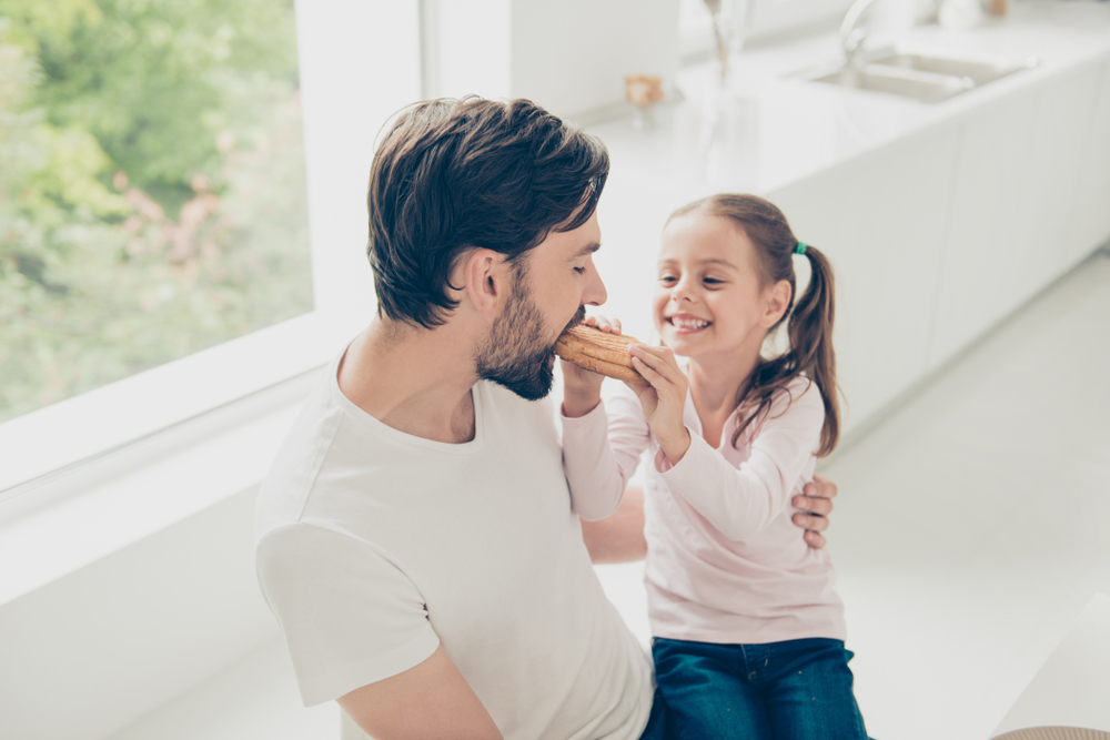 Nice adorable lovely daddy and adopted girl, enjoying tasty yummy snack on holiday, cheerful preteen girl with ponytails feeding dad, white light interior room