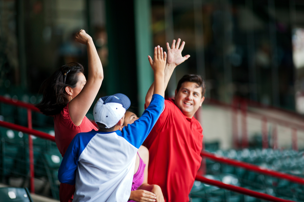Smiling father and son high fiving each other at a baseball game.