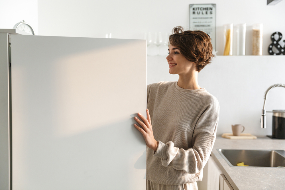 Happy young woman standing at the opened fridge