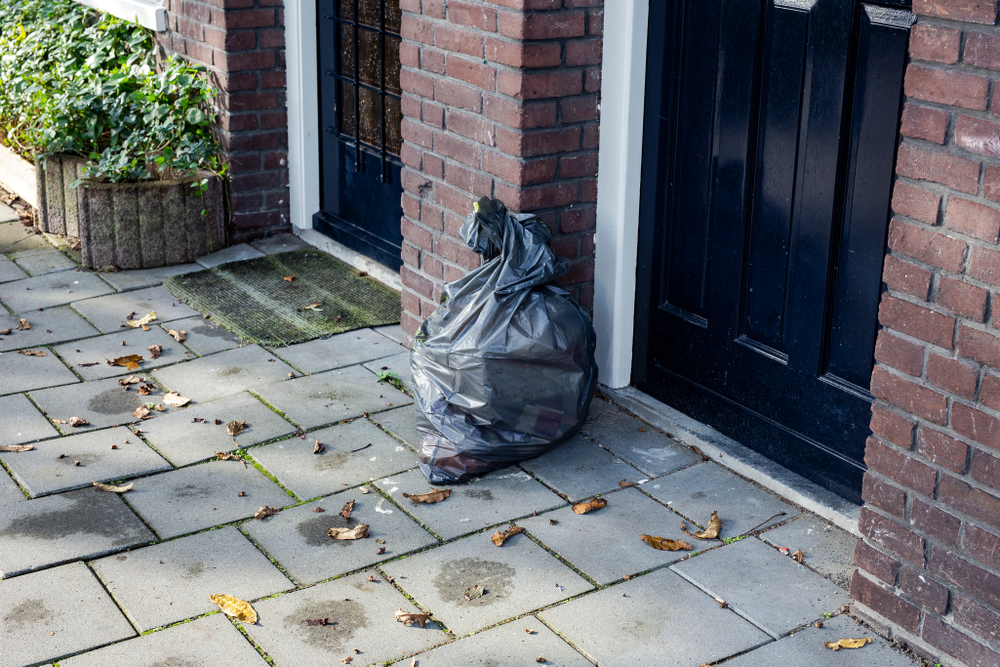 Garbage bag near a front door in a neighbourhood, ready for pick up closeup