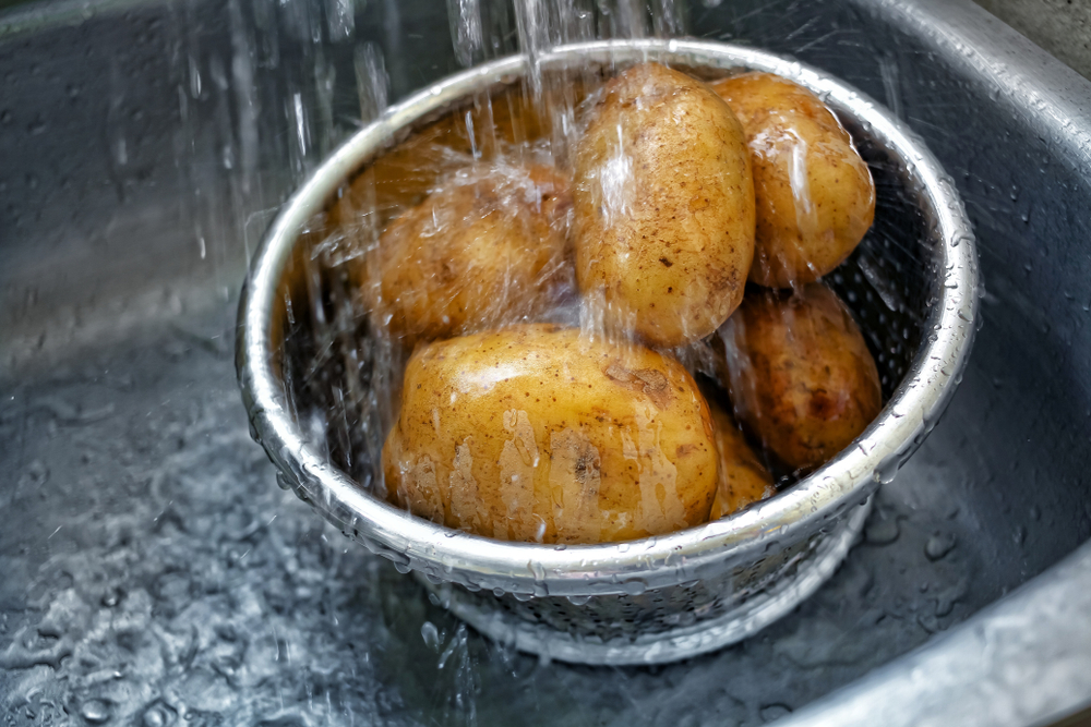 Potato washing, water rinsing in kitchen, potatoes in metal bowl, water splashed cleaning, copy space