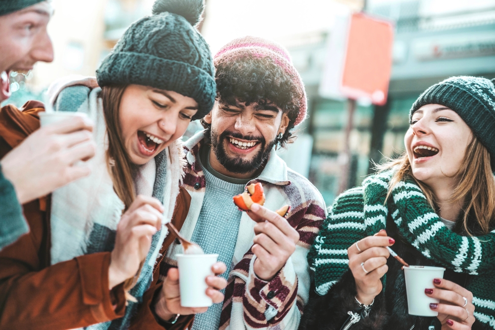 Happy friends having fun drinking mulled wine and hot chocolate at Christmas Market - Cheerful young people enjoying winter holidays on weekend vacation - Tourism lifestyle and friendship concept
