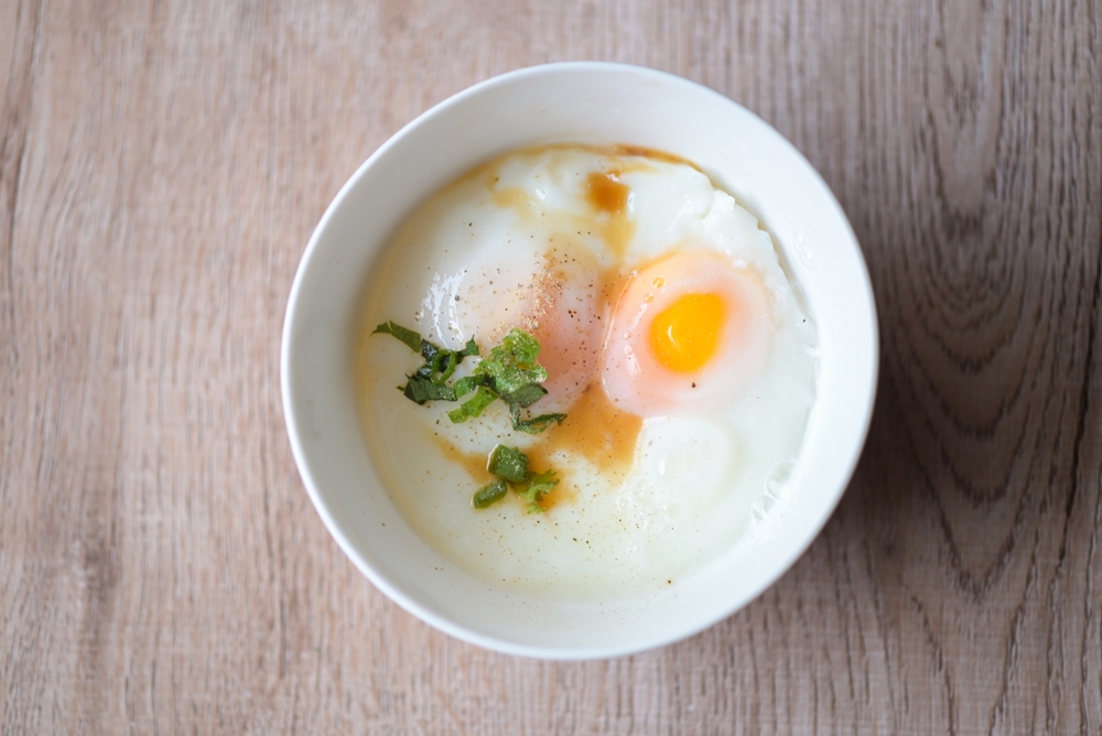 egg breakfast , soft-boiled eggs on white bowl with pepper, coriander on wooden table, Onsen tamago egg - egg microwave