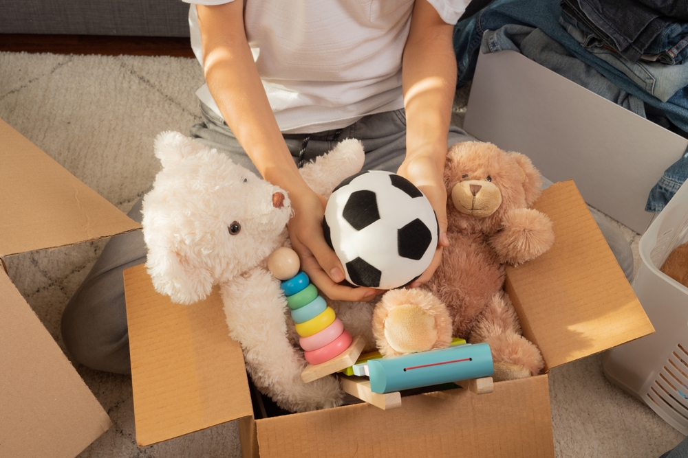 Teenager sorting and collect kid toys, clothes into boxes at home. Donations for charity, help low income families, declutter home, sell online, moving into new home, recycling, sustainable living