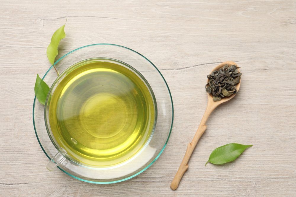 Refreshing green tea in cup, spoon and leaves on wooden table, flat lay