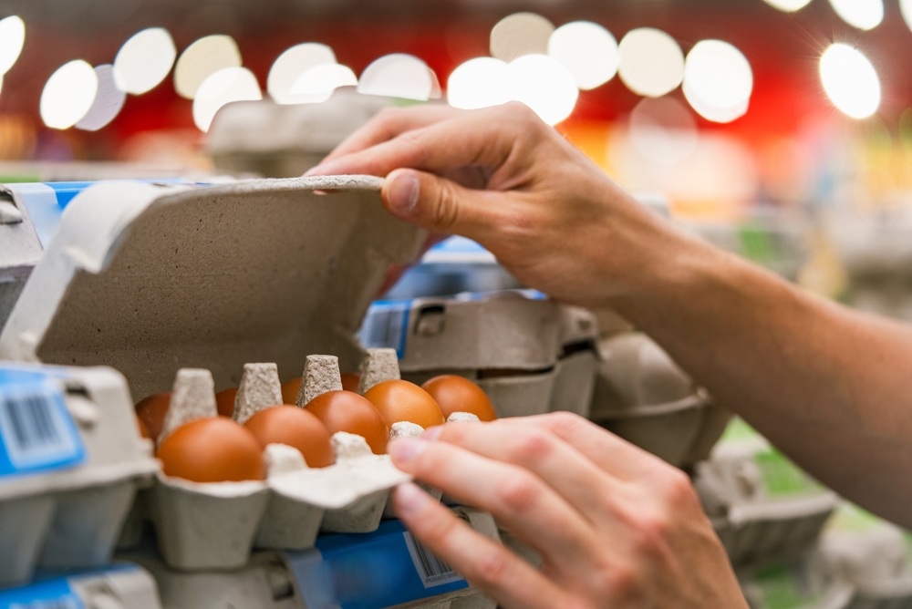 Man hands inspecting a carton of brown eggs in the supermarket aisle, ensuring quality and freshness. Selection of quality products in the store,
