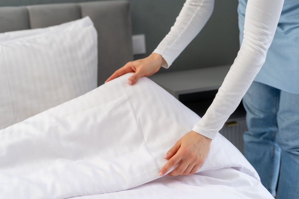 Close up view of woman make the bed in hotel bedroom,copy space on bedding. Maid hold white blanket with fresh duvet cover in hands. Room service, laundry day concepts