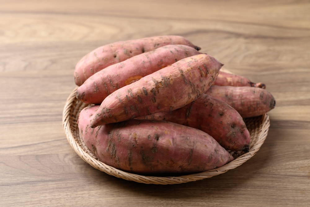 Raw organic Japanese sweet potatoes in basket on wooden background