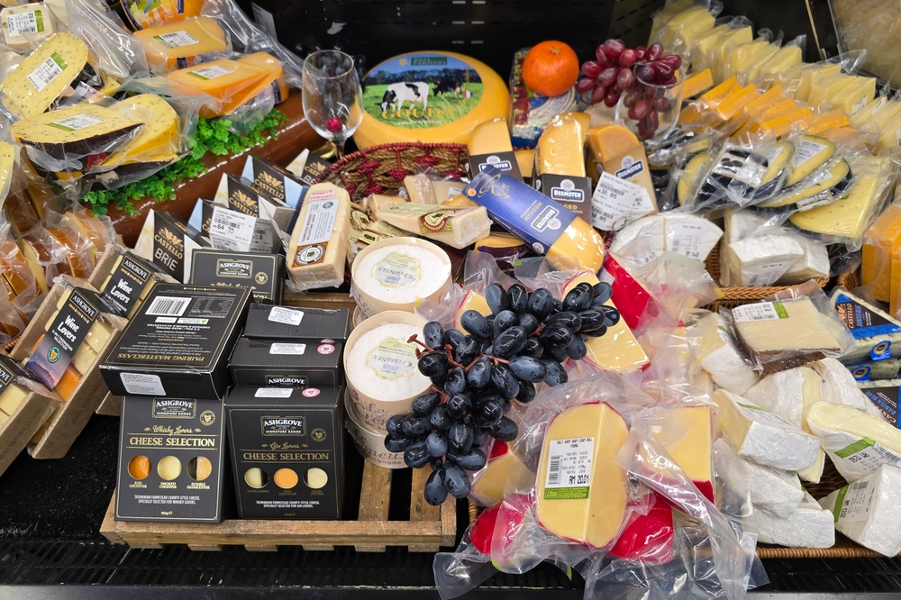 Bangsar, Malaysia – Mar 29, 2025: Various imported cheeses including gouda, brie, cheddar, wine-pairing sets, and black grapes on a rustic wooden display in a supermarket chill section.