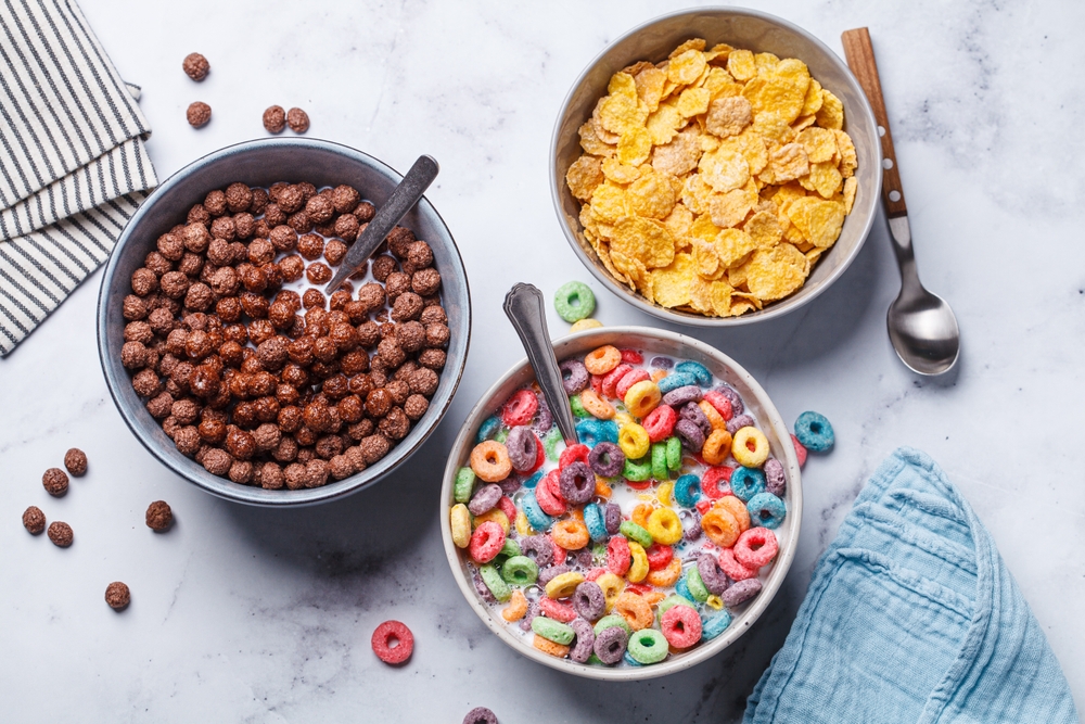 Different types of breakfast cereals background. Chocolate balls, cornflakes and colorful fruit rings on a white background, top view.