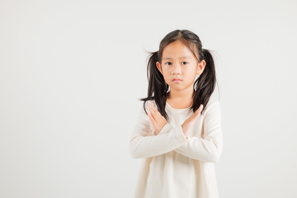 Portrait Asian young kid girl unhappy or confident standing holding two cross arms say no X sign, studio shot isolated white background, Thai kindergarten child pose reject gesture with copy space