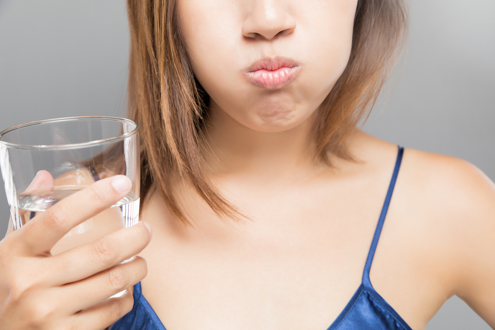 Woman rinsing and gargling while using mouthwash from a glass, During daily oral hygiene routine, Portrait with bare shoulders, Dental Health Concepts