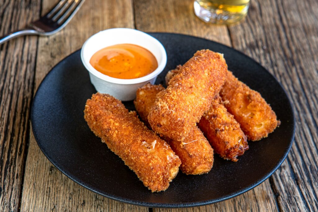 
A black plate topped with fried food next to a cup of dipping sauce
