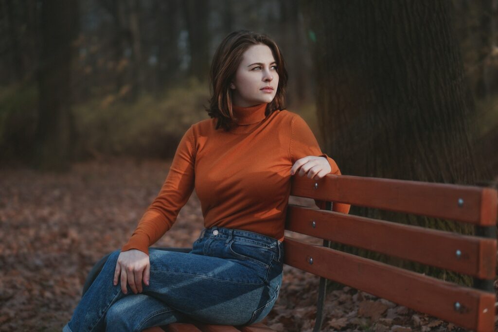 woman in red long sleeve shirt and blue denim jeans sitting on brown wooden bench