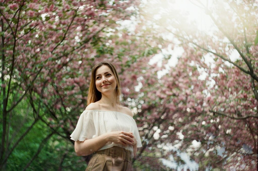woman in white dress standing under pink cherry blossom tree during daytime