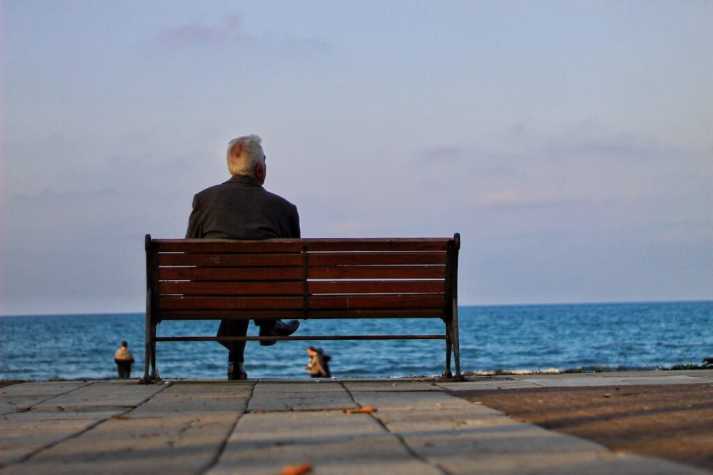 Unrecognizable old man sitting on bench on embankment
