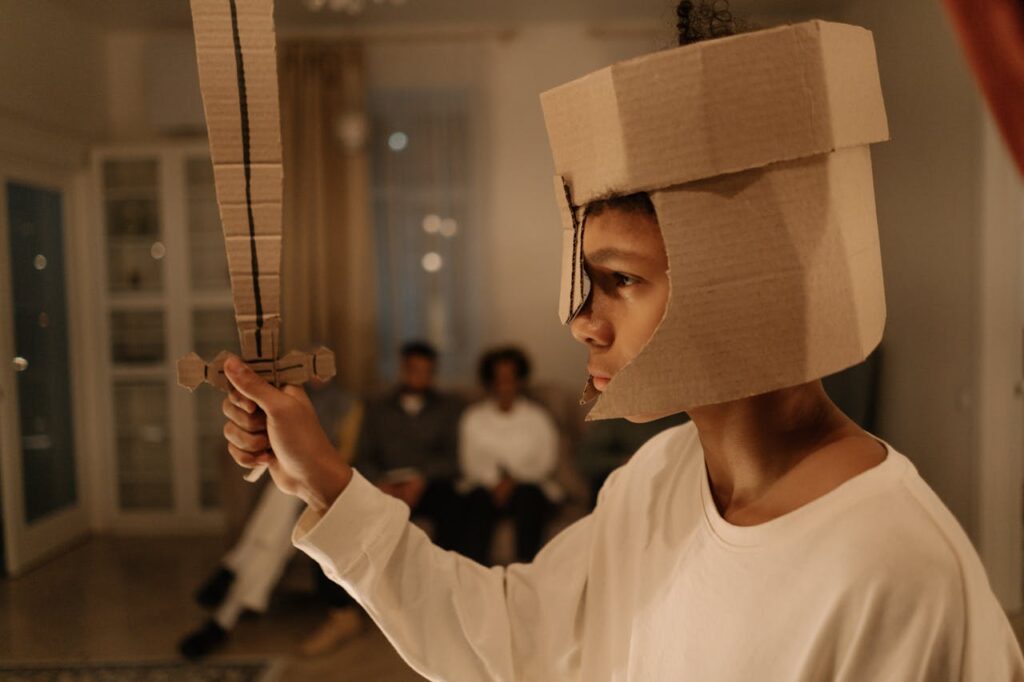 Boy in White Long Sleeve Shirt Holding Brown Cardboard Sword
