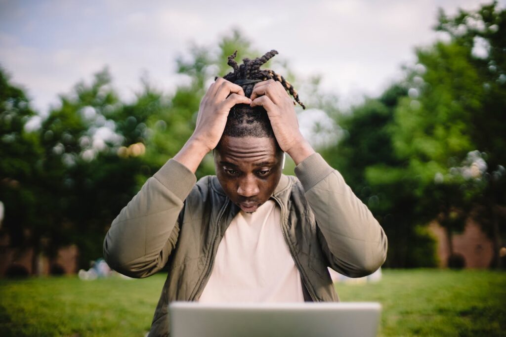 Stressed black male entrepreneur working on laptop in park
