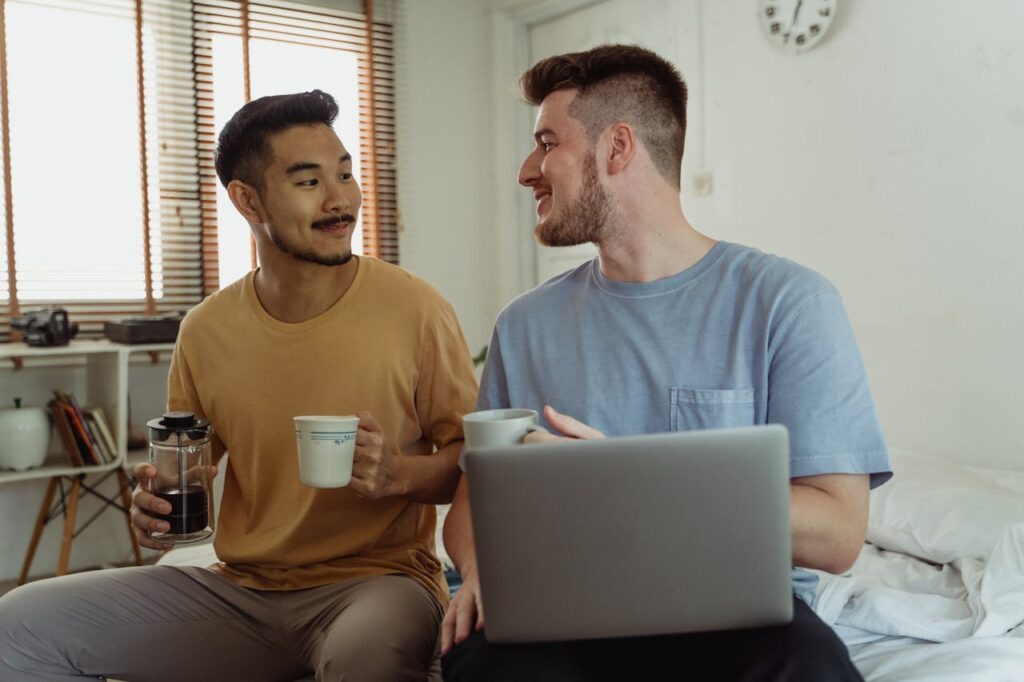 Men Talking, Drinking Coffee and Using Laptop in Bedroom
