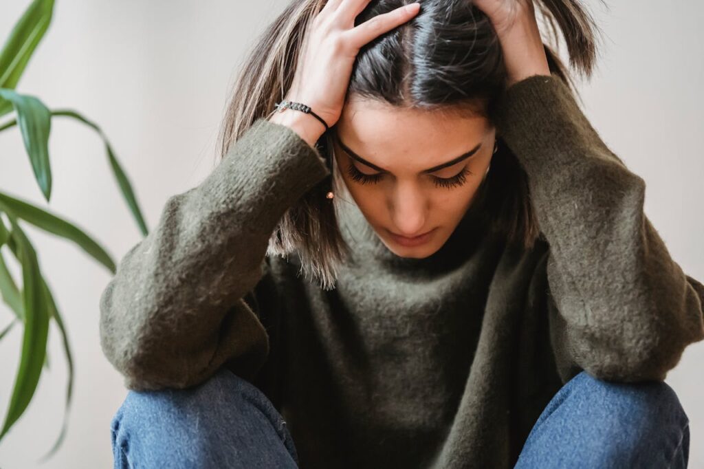 Depressed young ethnic lady touching head and looking down sitting near wall
