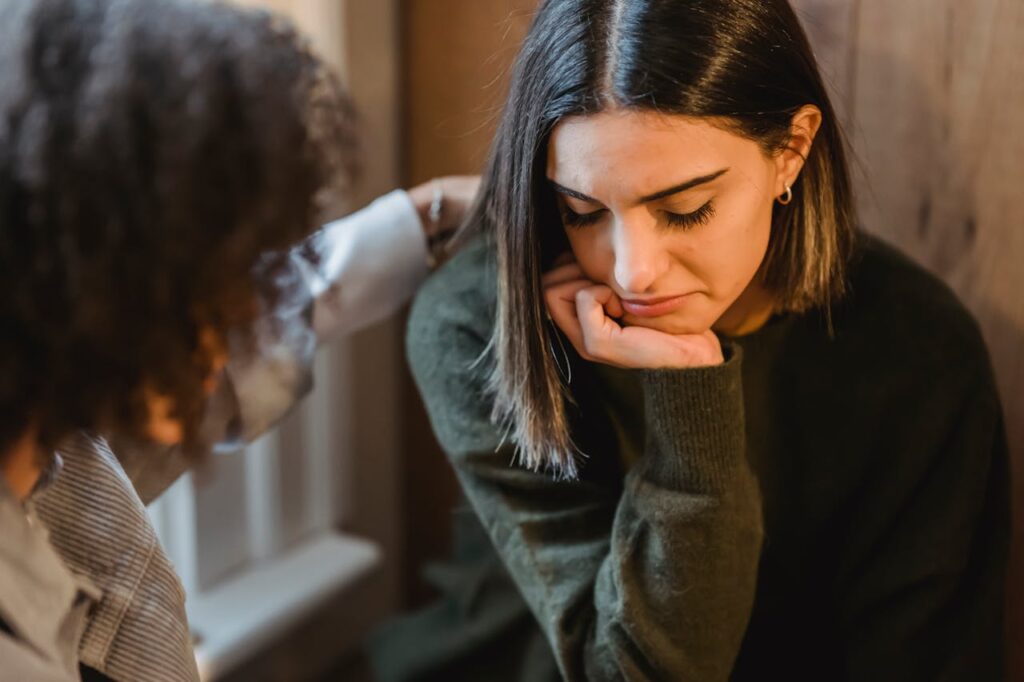 Crop woman tapping shoulder of frustrated female friend
