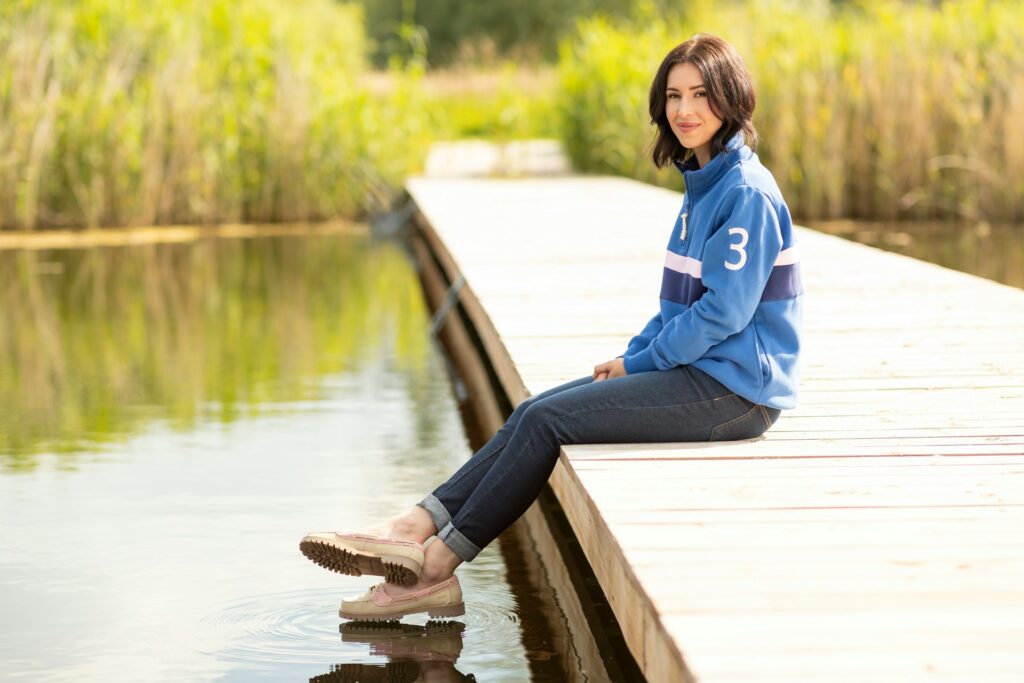 A woman sitting on a dock next to a body of water
