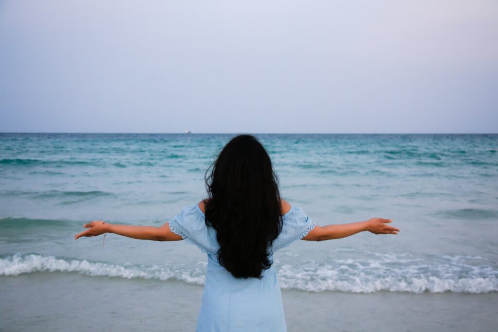 a woman standing on a beach with her arms outstretched