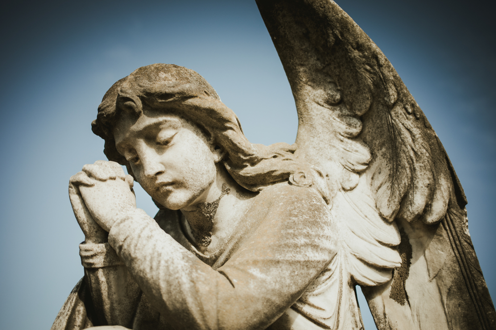 From below view of stone obsolete sculpture of angel praying in sorrow on cemetery tomb