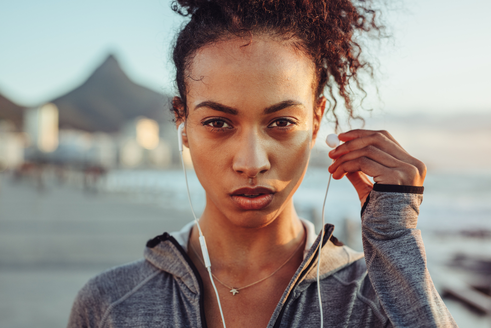 Close up of woman athlete wearing earphones outdoors. Female listening to music during workout.