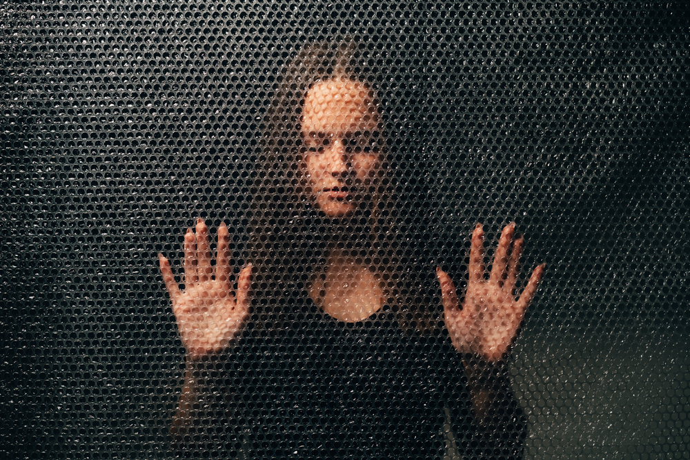 Peaceful woman. Soul healing. Spiritual practice. Esoteric mystery. Textured portrait of relaxed lady in black with closed eyes touching plastic bubble wrap wall in darkness.