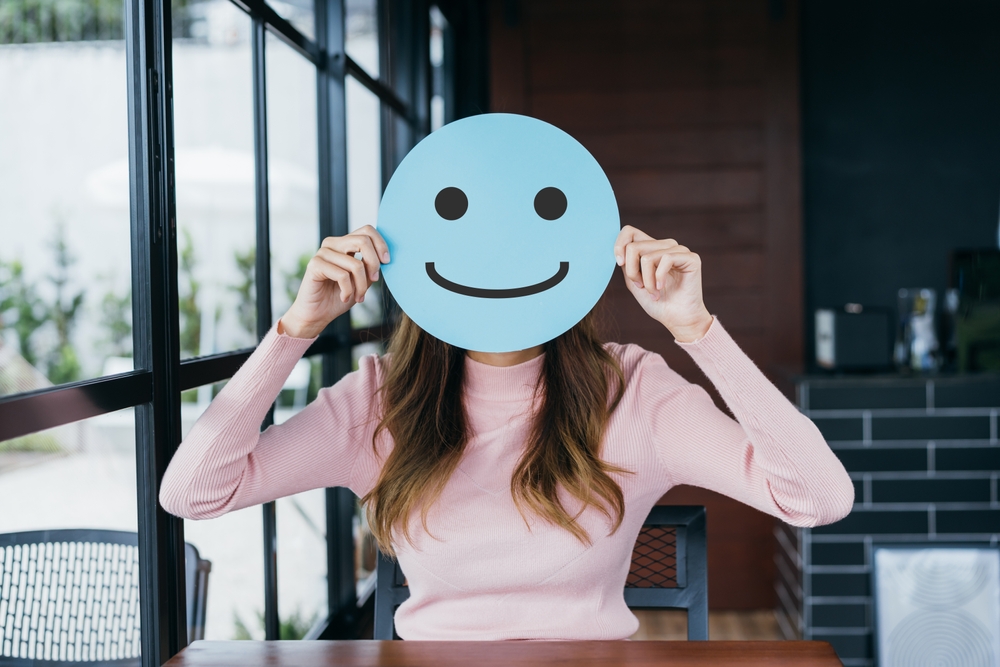 Asian woman holding blue happy smile face on paper cut, user giving good feedback rating, think positive , customer review, assessment, of mental health day, Compliment Day, satisfaction concept.