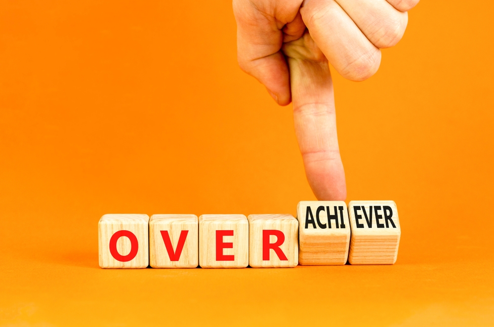 Achiever or overachiever symbol. Businessman turns wooden cubes and changes word Achiever to Overachiever. Beautiful orange background. Business achiever or overachiever concept. Copy space.