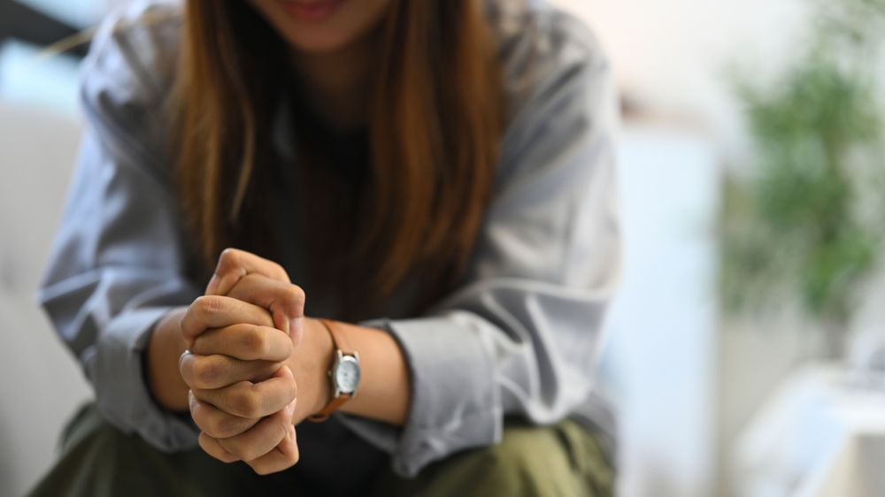 Depressed sad woman sitting alone on sofa with hands clasped. Mental health concept.