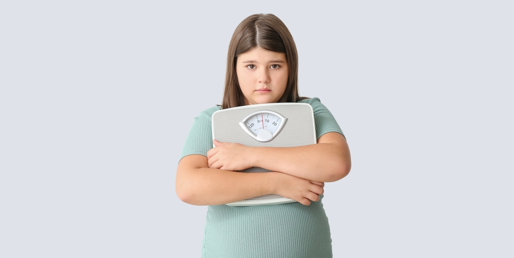 Sad overweight girl with measuring scales on light background