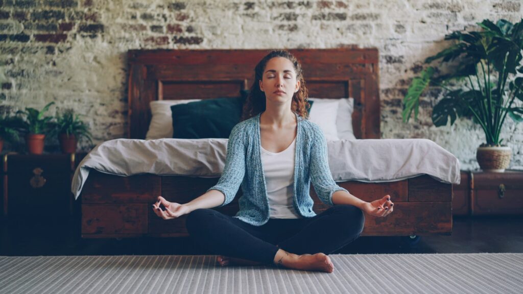 Woman meditating peacefully in a bedroom.
