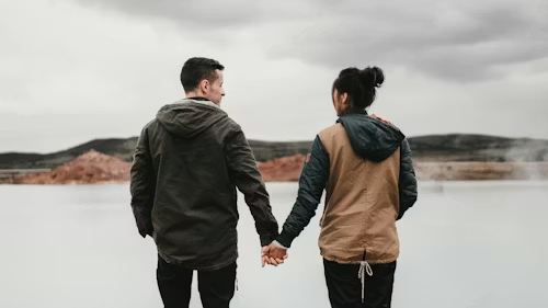 Couple holding hands facing a lake.