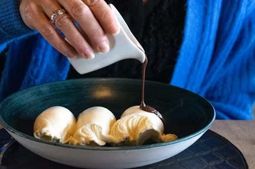 a-person-pouring-chocolate-sauce-on-some-food-in-a-bowl
