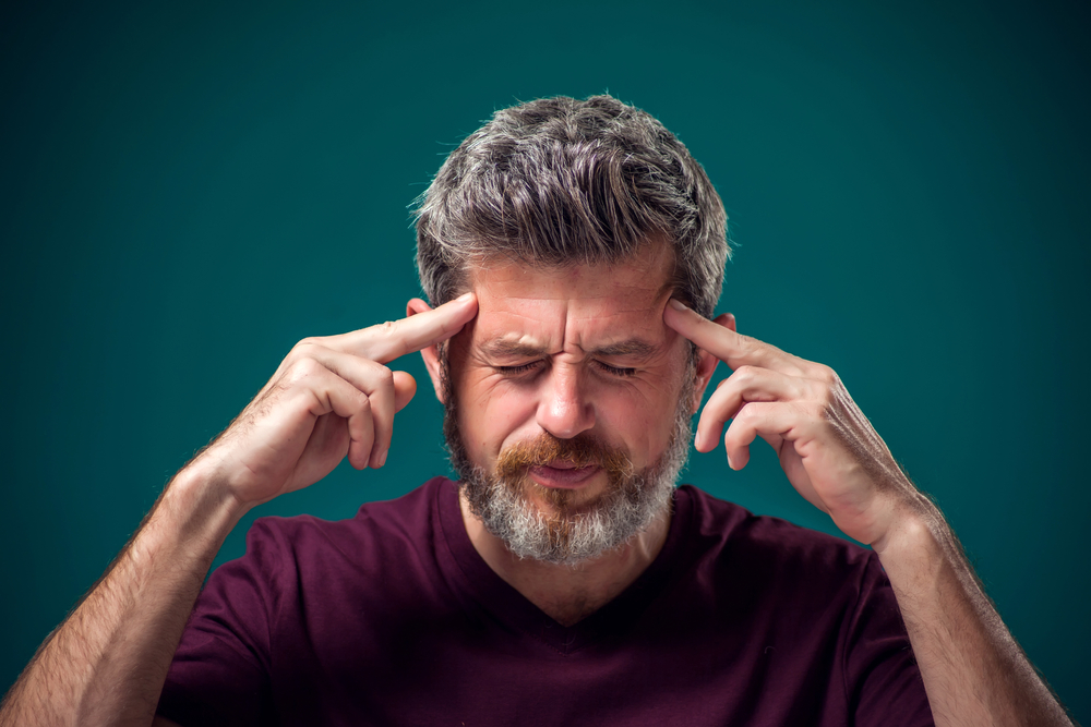 A portrait of bearded man in red t-shirt thinking hard or have headache. People, emotions and health concept