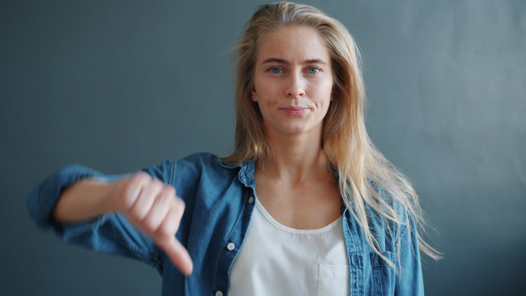 Confident young woman displaying a thumbs down sign against a neutral background.
