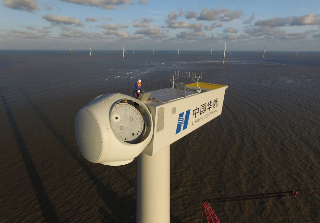 An engineer performs maintenance on an offshore wind turbine, under clear skies.