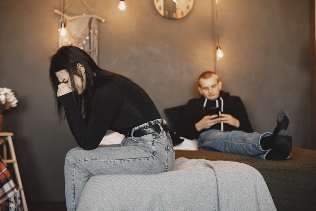 woman in black shirt sitting on bed with man looking at his phone